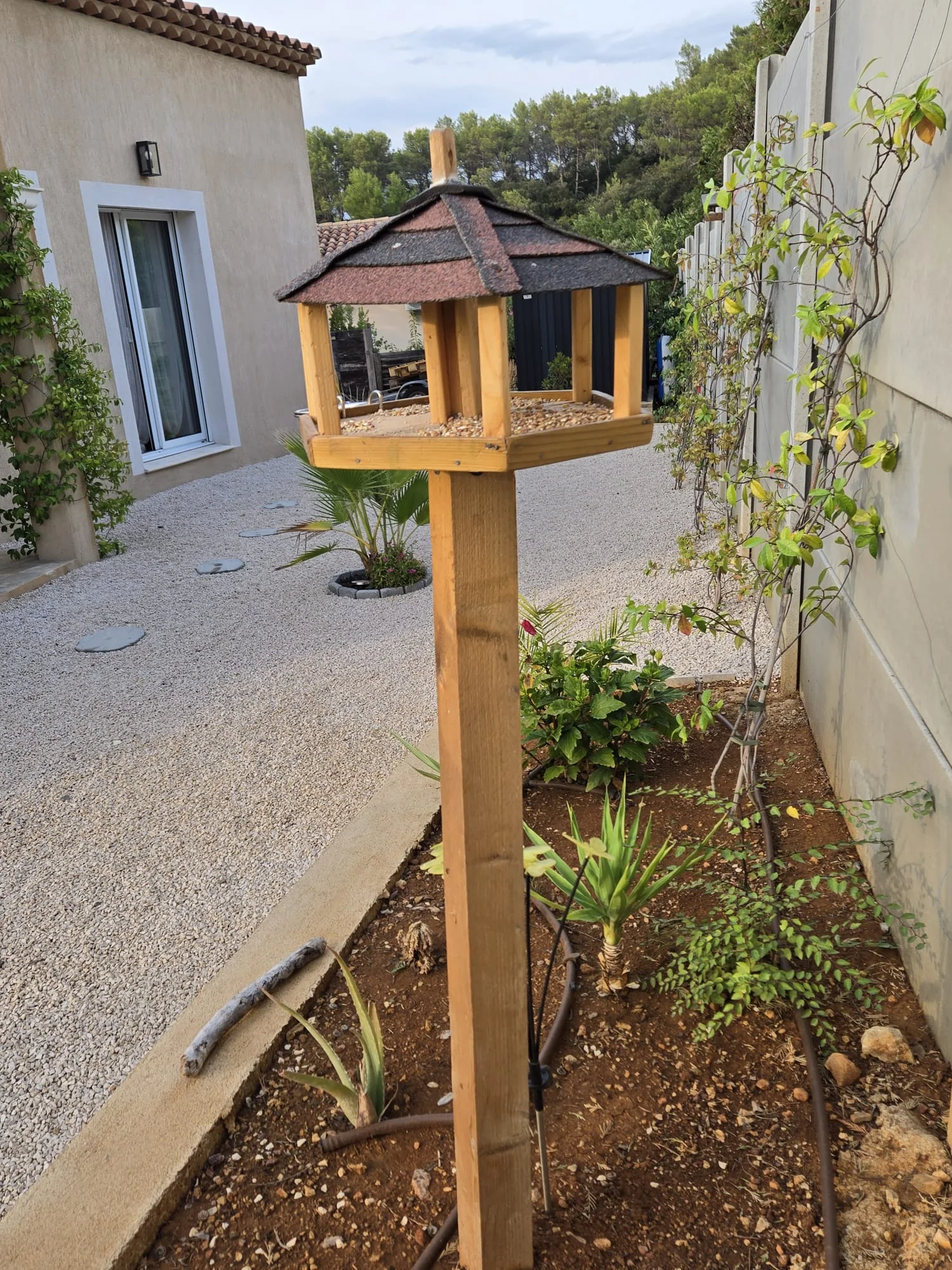 Mangeoire La Jardinière installée sur un pied près d’une maison